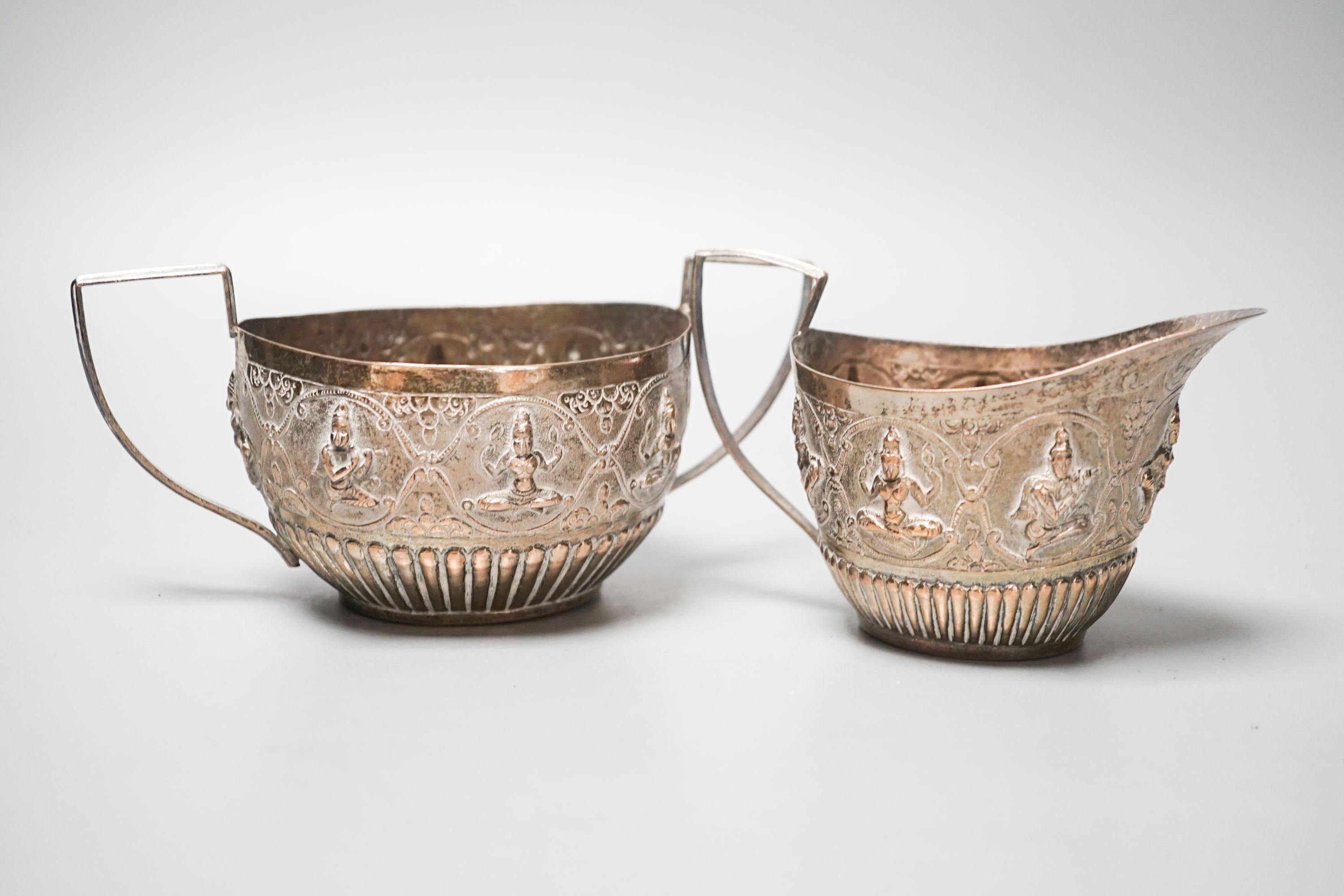 An Indian white metal sugar bowl and cream jug, embossed with deities, 8.5oz.